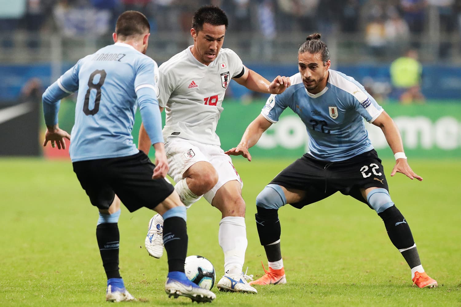 Shinji Okazaki, do Japão, é marcado pelos jogadores uruguaios Martín Cáceres e Nahitan Nández, durante partida válida pela Copa América