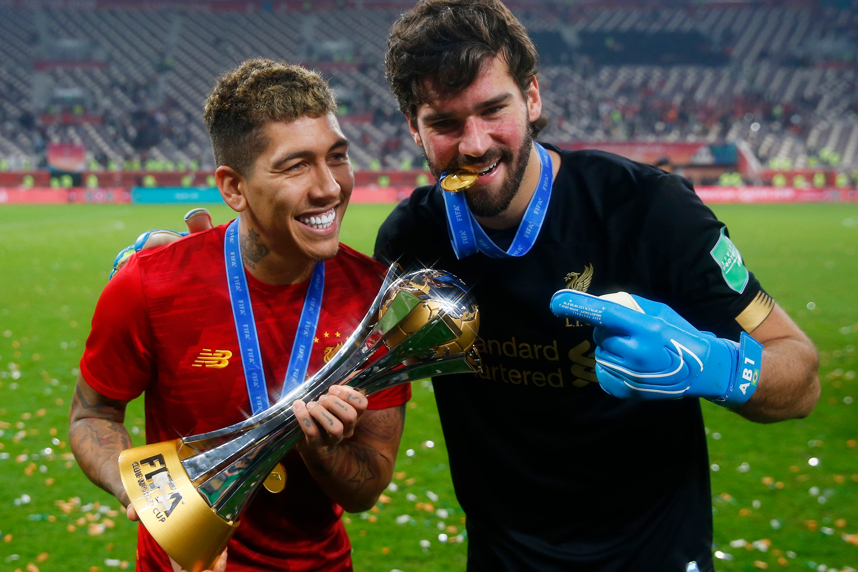 Roberto Firmino empunha a taça do Mundial do clube ao lado do goleiro brasileiro Alisson, do Liverpool