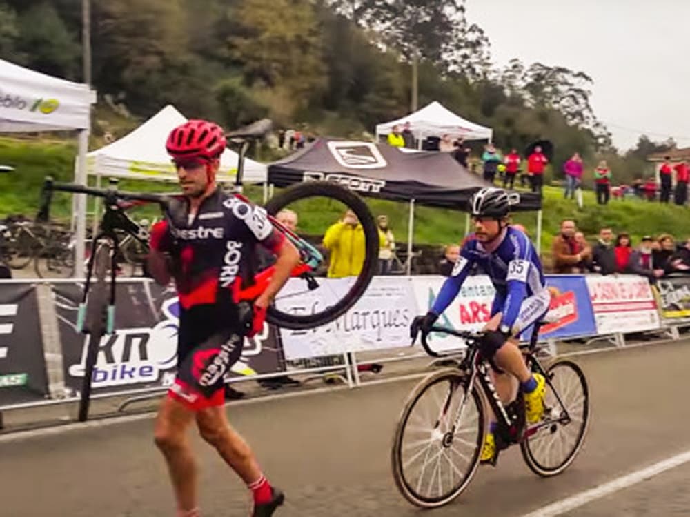 Ismael Esteban carrega bike com pneu furado, enquanto Agustín Navarro apenas o acompanha e o deixa ganhar medalha de bronze em competição de ciclismo na Espanha