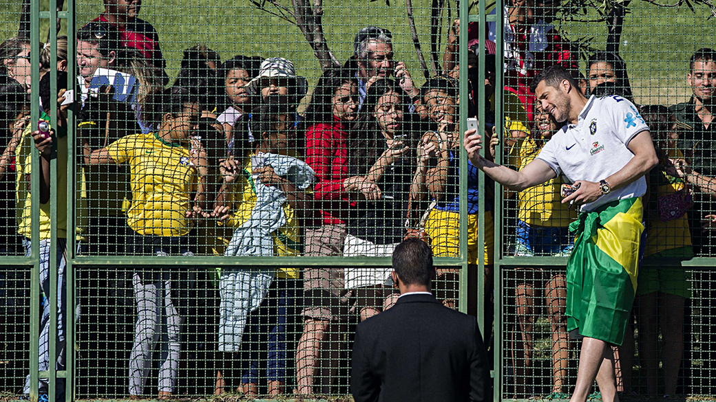 O goleiro Júlio César, da Seleção Brasileira, atende a pedidos de torcedores e se dirige à cerca de um hotel, em Brasília, com bandeira do Brasil amarrada na cintura após ganhá-la de um torcedor